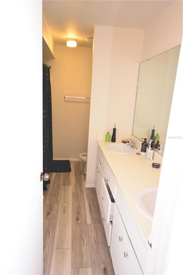 full bathroom featuring double vanity, toilet, a sink, wood finished floors, and baseboards