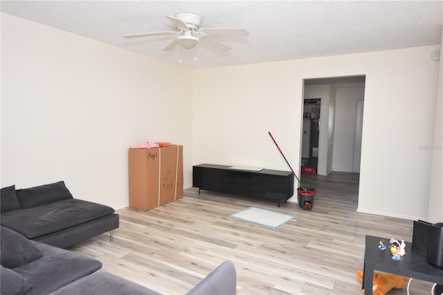 living area with a textured ceiling, baseboards, a ceiling fan, and light wood-style floors