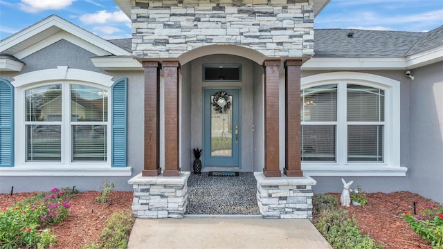 entrance to property with stucco siding, brick siding, and roof with shingles