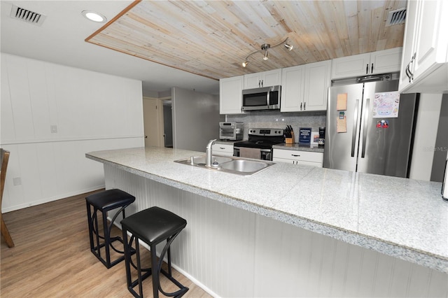 kitchen featuring a breakfast bar area, stainless steel appliances, light countertops, white cabinetry, and a peninsula