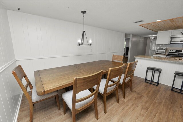 dining area with light wood-style floors, a toaster, visible vents, and an inviting chandelier