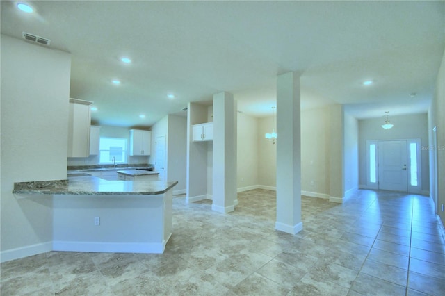 kitchen featuring a peninsula, a sink, visible vents, white cabinets, and dark stone counters