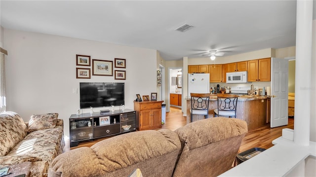 living room featuring ceiling fan, light wood finished floors, and visible vents