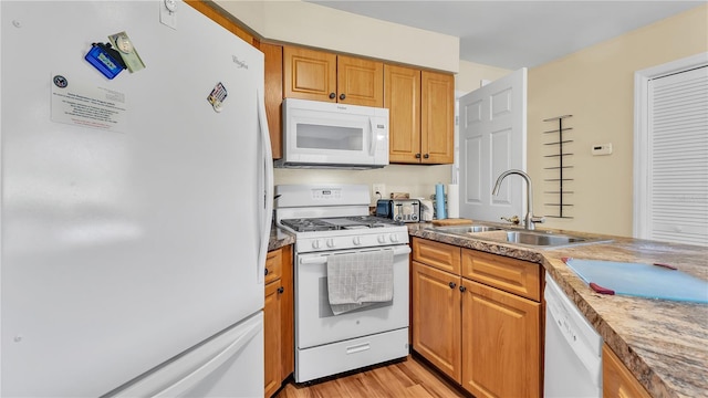 kitchen featuring white appliances, a sink, light wood-style flooring, and brown cabinets