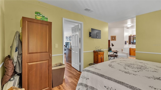 bedroom with light wood-style floors, ensuite bath, and visible vents