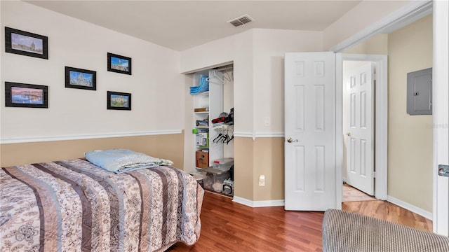 bedroom featuring electric panel, visible vents, baseboards, and wood finished floors