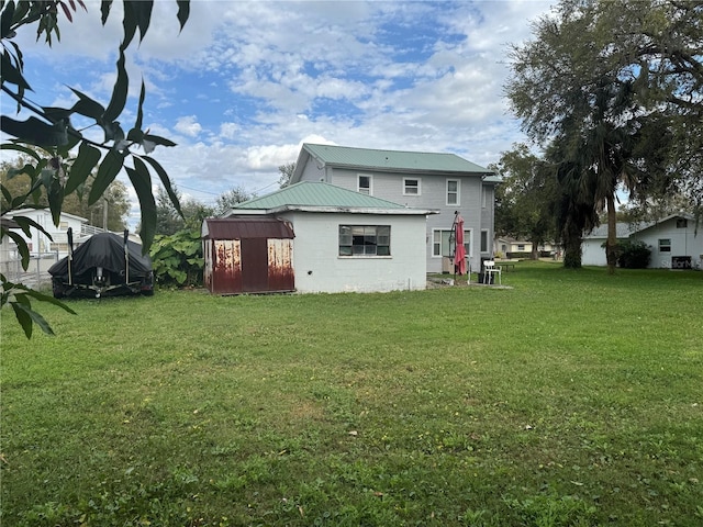 rear view of property with metal roof, a storage shed, an outdoor structure, concrete block siding, and a yard