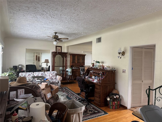 living room with light wood-style flooring, visible vents, ceiling fan, and a textured ceiling