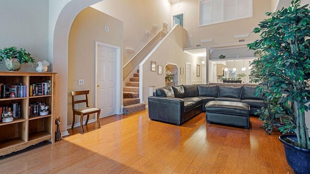 living area with a towering ceiling, stairs, arched walkways, and wood finished floors