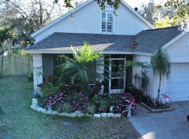 view of front of home featuring roof with shingles, fence, an attached garage, and stucco siding