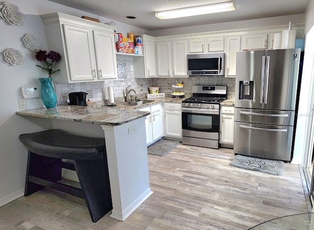 kitchen featuring light stone counters, stainless steel appliances, a peninsula, white cabinets, and tasteful backsplash