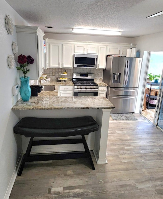 kitchen featuring light stone counters, stainless steel appliances, a breakfast bar, a peninsula, and white cabinets