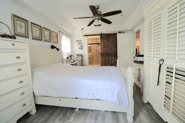 bedroom featuring ceiling fan, a raised ceiling, dark wood finished floors, and a barn door