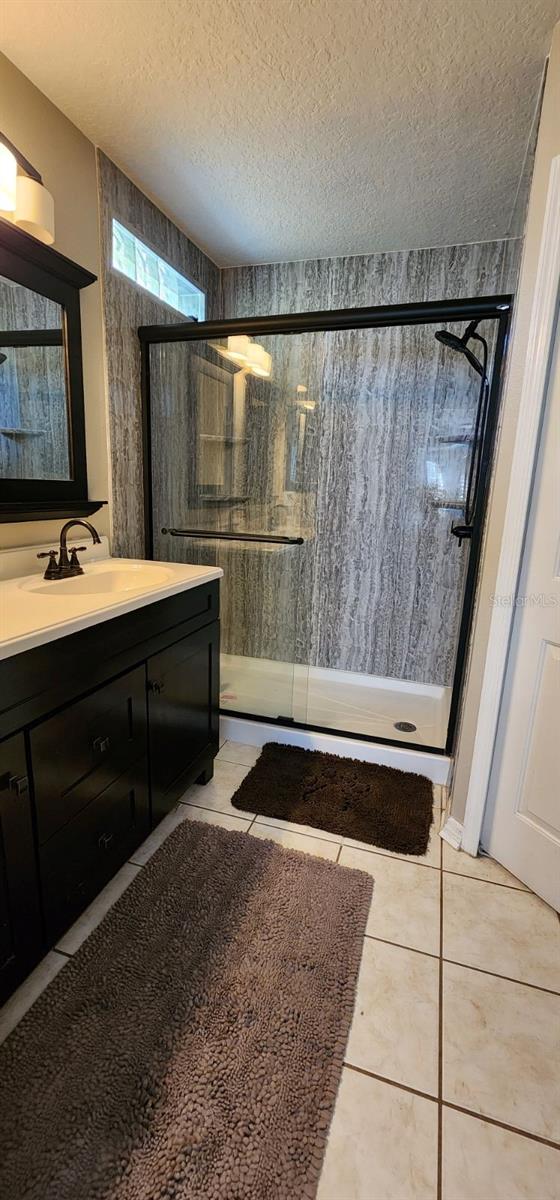 full bathroom with a stall shower, vanity, a textured ceiling, and tile patterned floors