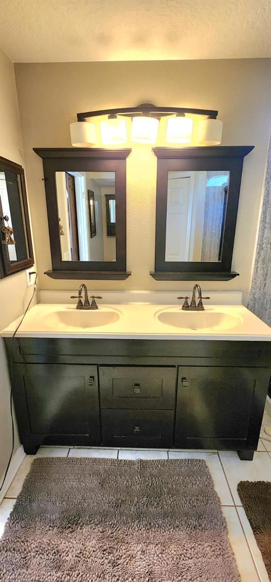 full bath featuring double vanity, tile patterned flooring, a textured ceiling, and a sink