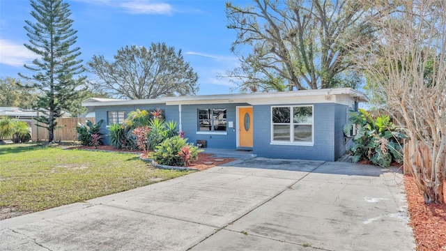 view of front of house with concrete driveway, a front yard, concrete block siding, and fence