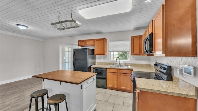 kitchen featuring a breakfast bar, a sink, light countertops, black appliances, and brown cabinetry