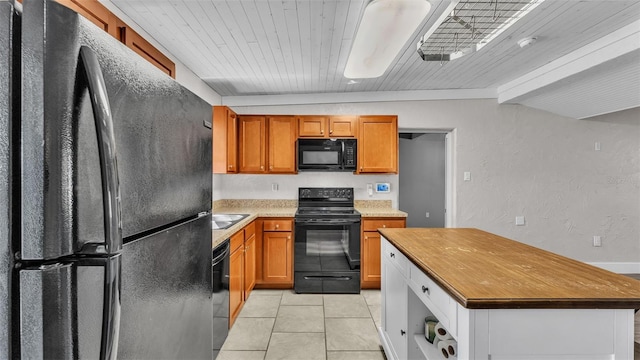 kitchen with light countertops, a textured wall, brown cabinetry, light tile patterned flooring, and black appliances