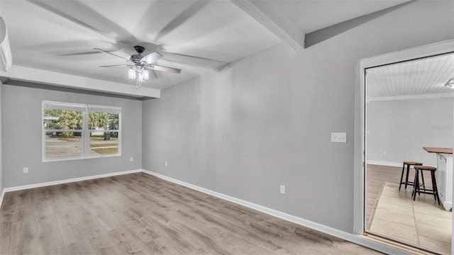 empty room featuring beam ceiling, light wood-type flooring, a ceiling fan, and baseboards