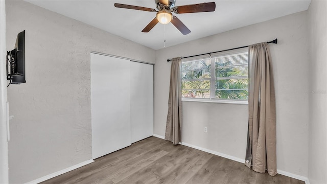 unfurnished bedroom with a textured wall, a ceiling fan, baseboards, light wood-style floors, and a closet