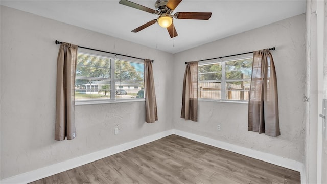 spare room featuring a ceiling fan, a textured wall, baseboards, and wood finished floors