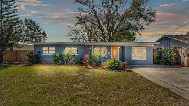 ranch-style house with a yard, concrete driveway, concrete block siding, and fence