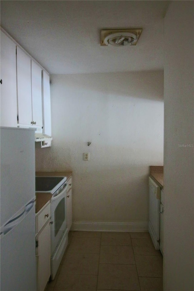 kitchen with light tile patterned floors, baseboards, white appliances, and white cabinets