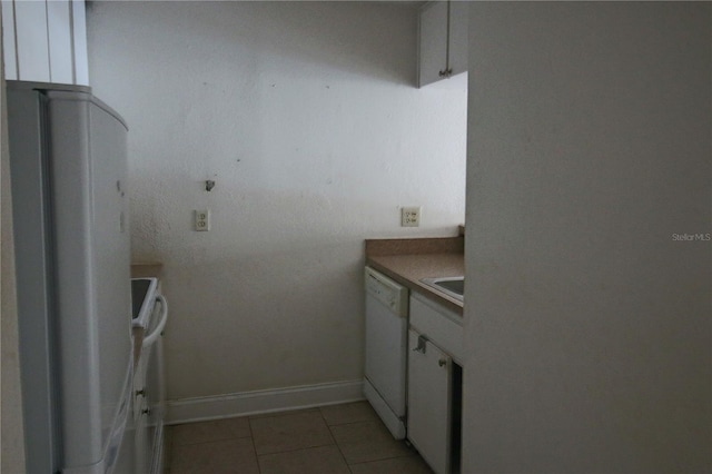 kitchen with baseboards, dishwasher, light tile patterned floors, stove, and white cabinets