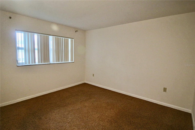 unfurnished room with baseboards and dark colored carpet