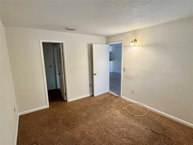 unfurnished bedroom with visible vents, a textured ceiling, carpet flooring, baseboards, and a textured wall