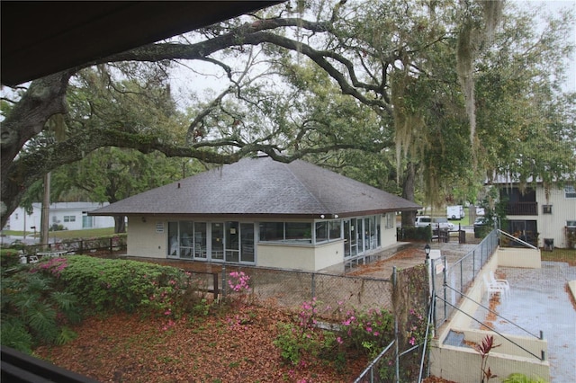 back of house with stucco siding, roof with shingles, and fence