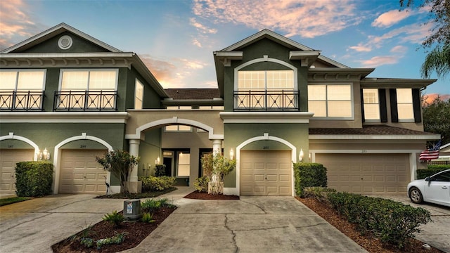 view of front facade featuring driveway, a balcony, an attached garage, and stucco siding