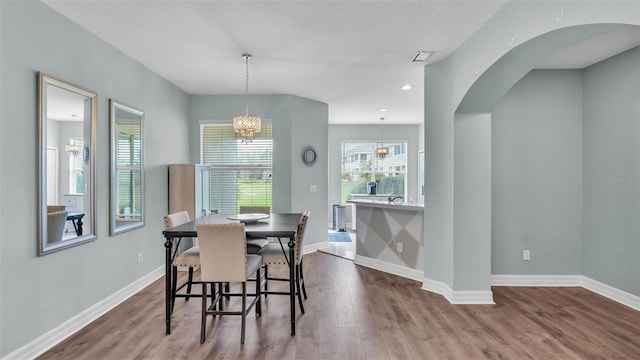 dining space featuring light wood finished floors, baseboards, arched walkways, and a notable chandelier