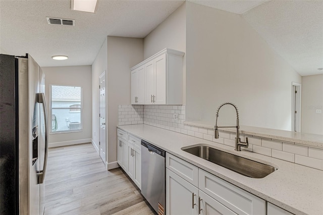 kitchen with visible vents, appliances with stainless steel finishes, light stone countertops, white cabinetry, and a sink