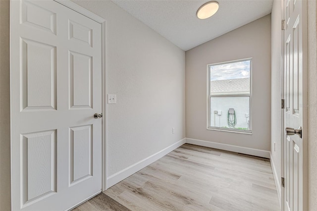 unfurnished room featuring lofted ceiling, a textured ceiling, light wood-type flooring, and baseboards