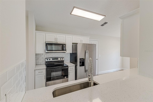 kitchen featuring white cabinets, appliances with stainless steel finishes, a sink, light stone countertops, and backsplash