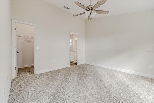 unfurnished bedroom featuring baseboards, a walk in closet, visible vents, and light colored carpet