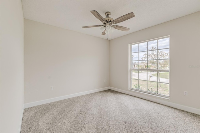 carpeted spare room featuring baseboards and a ceiling fan