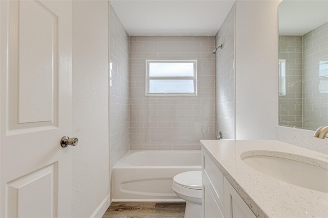 bathroom with a textured wall, toilet, wood finished floors,  shower combination, and vanity