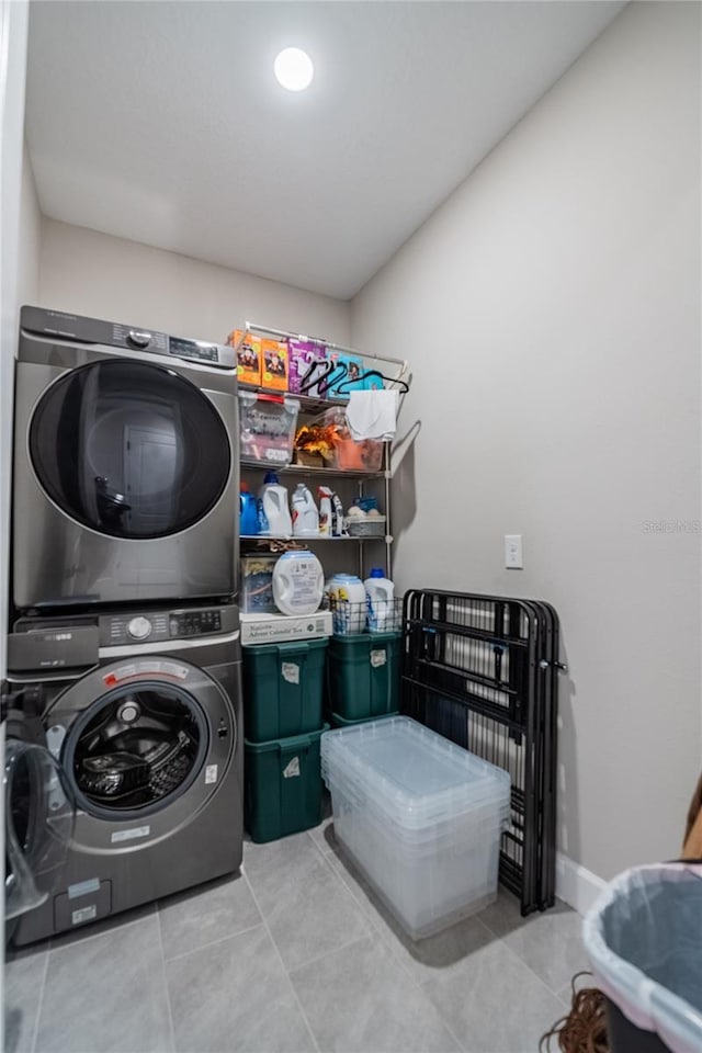 clothes washing area featuring tile patterned floors, stacked washer / drying machine, baseboards, and laundry area