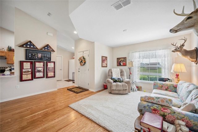 living room with visible vents, vaulted ceiling, baseboards, and wood finished floors