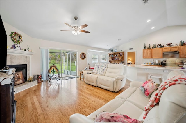 living room featuring a fireplace, visible vents, a ceiling fan, vaulted ceiling, and light wood-type flooring