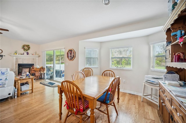 dining space with light wood-type flooring, plenty of natural light, baseboards, and a tile fireplace