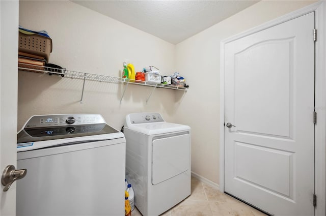 clothes washing area featuring washer and dryer, laundry area, light tile patterned flooring, and baseboards