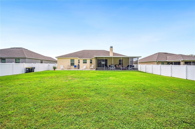 rear view of property with a fenced backyard, a chimney, a lawn, and a patio