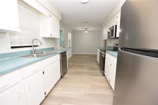 kitchen featuring appliances with stainless steel finishes, light wood-type flooring, a sink, and white cabinets