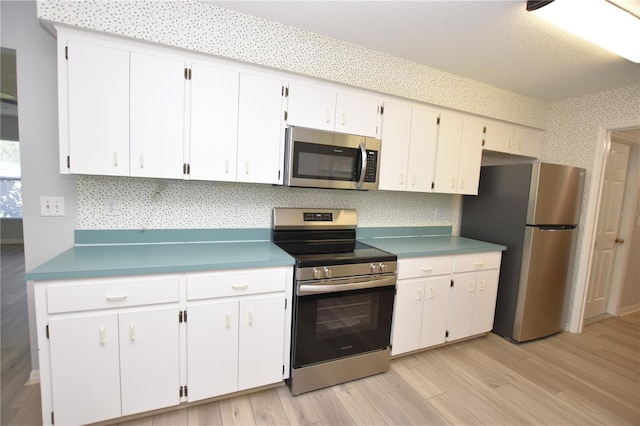 kitchen with stainless steel appliances, white cabinets, light wood-style floors, light countertops, and wallpapered walls