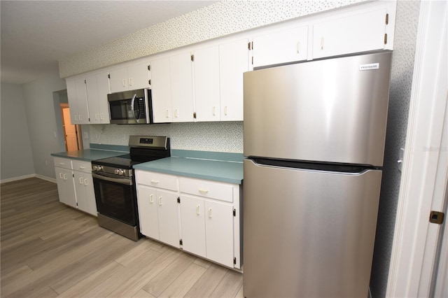 kitchen featuring baseboards, decorative backsplash, appliances with stainless steel finishes, light wood-type flooring, and white cabinetry