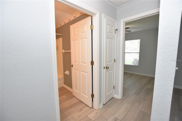 hall featuring light wood-type flooring, baseboards, and a textured wall