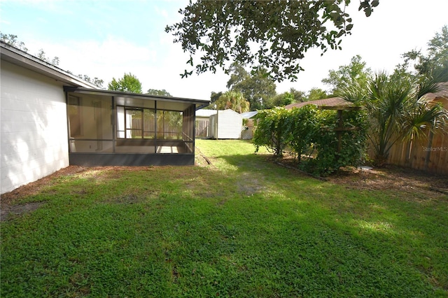 view of yard with a sunroom, a fenced backyard, a storage unit, and an outbuilding